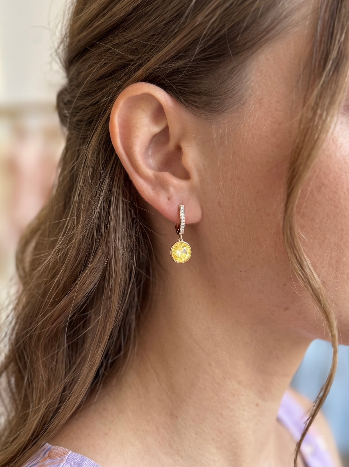 Sieviete ar 18K apzeltītiem auskariem "Merveille", ko rotā liels dzeltens Swarovski kristāls un smalki cirkoni.